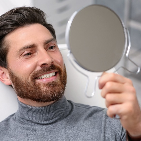Man looking at his smile in the mirror at the dentist’s office