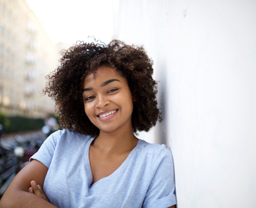 Woman smiling and leaning against wall after getting tooth-colored fillings in Derby, KS