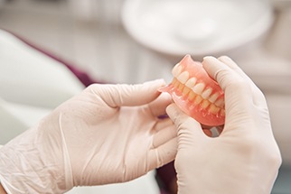 A dentist with gloved hands holding a pair of dentures