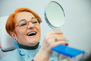 A smiling older woman admiring her new dentures