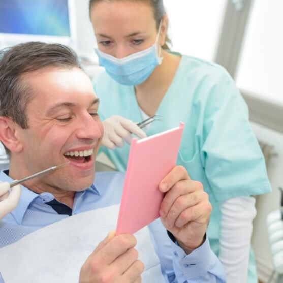 Man looking at smile after tooth replacement with dental bridge