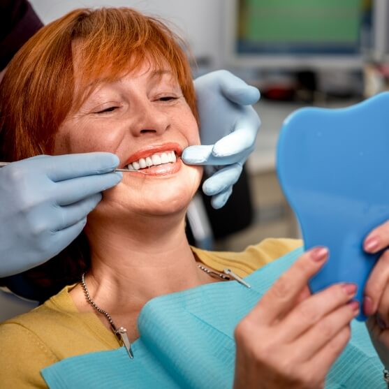 Woman looking at smile after tooth replacement with dental implants